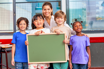 Multi ethnic primary elementary classmates with teacher holding green chalkboard