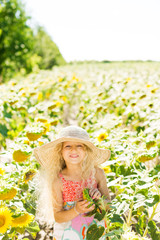 Fototapeta na wymiar Little girl with curly white hair in a field of sunflowers. Girl in a straw hat and sarafan