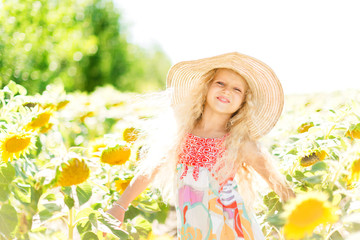 Little girl with curly white hair in a field of sunflowers. Girl in a straw hat and sarafan