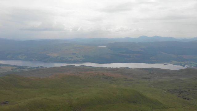 An aerial forward footage of a grassy mountain plateau with a huge lake and mountain range in the background under a cloudy sky	