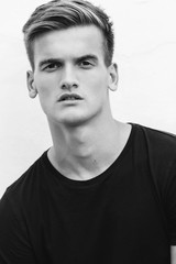 Portrait of a stylish young blond man in a black t-shirt on a white background.