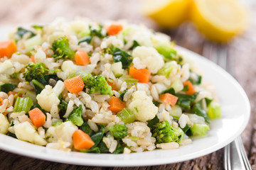 Fresh cooked brown rice with steamed vegetables (broccoli, cauliflower, swiss chard, carrot, celery) on plate, lemon in the back (Selective Focus, Focus one third into the plate)