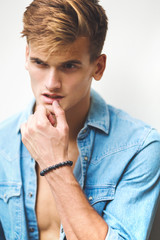 Portrait of a stylish young blond man in a denim look on a white background.