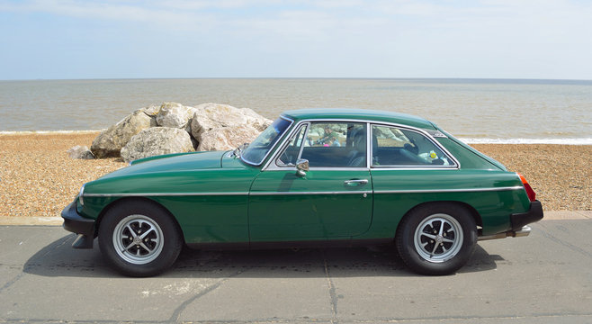  Classic Racing Green MGB GT parked on seafront promenade.