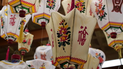 A group of old traditional Chinese lanterns hangs in a dusty antique warehouse, they're full of the beautiful script, colour & patterns. 