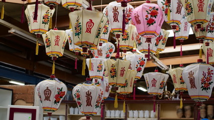 A group of old traditional Chinese lanterns hangs in a dusty antique warehouse, they're full of the beautiful script, colour & patterns. 