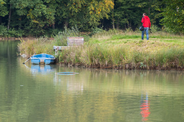 Fototapeta na wymiar un homme en rouge marche au bord de l'eau et regarde une barque bleue