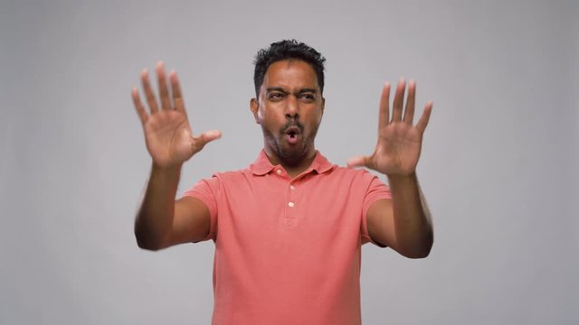 people concept - smiling young indian man making faces and different gestures with movements over grey background