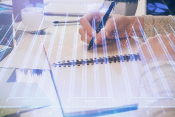 Forex chart hologram on hand taking notes background. Concept of analysis. Double exposure