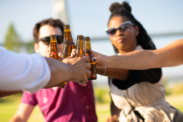Multiethnic team of friends celebrating outdoors. Hands of young men and women holding bottles, toasting, drinking beer. Party concept