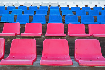 Naklejka premium Several rows of plastic seats in red, blue and white colors in the color of the russian flag, mounted on brown-painted wooden platforms on the podium of the village stadium in the russian outback