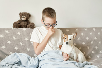 child boy with dog jack russell terrier sitting on the couch, the boy has a cold