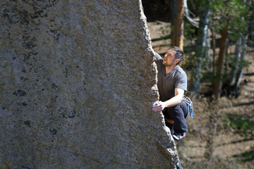 a young man climbs a steep cliff on the background of the forest. summer day. horizontal frame