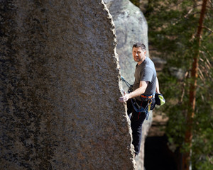 climber climbs a steep rock on the background of the forest. summer day. close up