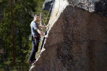 climber resting at an altitude of climbing a steep cliff. against the forest and lake. summer day.