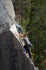 climber climbs a steep rock on the background of the forest. summer day. vertical frame