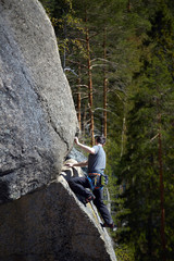 climber climbs a steep rock on the background of the forest. summer day. vertical frame