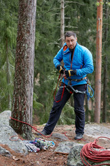 climber in a blue jacket with his equipment is preparing to descend. on the background of the forest. autumn