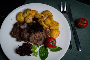 Meat medallions with potatoes at home, on a white plate. 