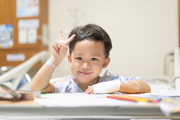 The patient boy is painting the paper with a color pencil in the hospital.