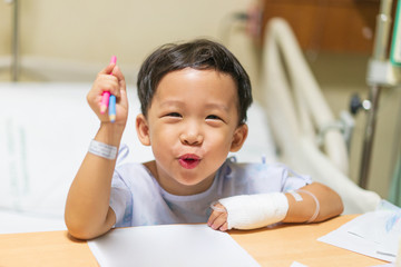 The patient boy is painting the paper with a color pencil in the hospital.