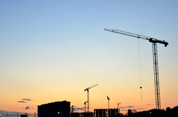 Jib construction tower cranes at a construction site on the sunset and blue sky background - Image