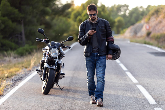 Man biker walking on the road while using her mobile phone after having suffered a breakdown on the road.