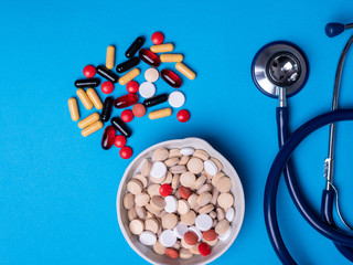 Top view with multicolored pills and capsules next to a stethoscope and a pill bowl