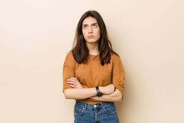 Young brunette woman against a beige background tired of a repetitive task.