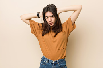 Young brunette woman against a beige background covering ears with hands trying not to hear too loud sound.