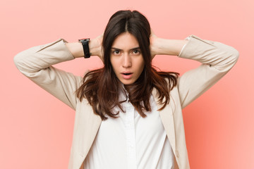 Young brunette business woman against a pink background covering ears with hands trying not to hear too loud sound.
