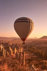 Foto op Plexiglas Bruin witte grote luchtballon stijgt in de lucht boven rotsen in Cappadocië