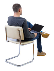 Back view of a man who sits on a chair with a laptop.