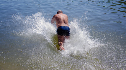 The guy jumps into the lake, splashing water