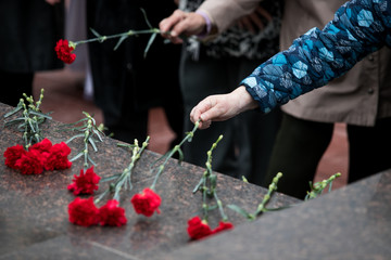 Red roses and carnation symbol of mourning - laying flowers to the monument, telephoto