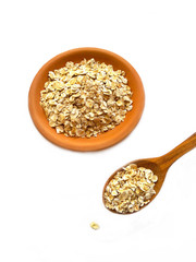 Raw Oats scattered from clay bowl and wooden spoon on white background. Oat flakes uncooked in ceramic plate and wooden spoon isolated on white. Concept of healthy eating vegan food. 