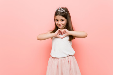 Little girl wearing a princess look smiling and showing a heart shape with hands. © Asier