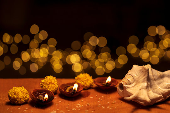 Lit Clay Diya In A Row With Bokeh On Diwali. Diwali diya clay lamps decorated with flowers and shankha burning or glowing on a wooden background isolated in black with bokeh lights and copy space.