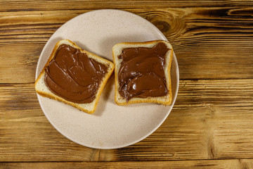 Two slices of bread with delicious chocolate hazelnut spread on wooden table. Top view