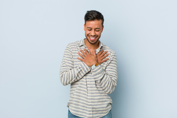 Young handsome filipino man laughing keeping hands on heart, concept of happiness.