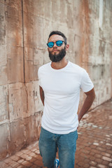 Young hipster man with beard wearing white blank t-shirt and blue jeans outdoor.