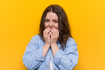 Young curvy plus size woman laughing about something, covering mouth with hands.