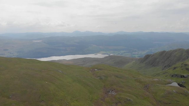 An aerial forward footage of a grassy mountain plateau with a huge lake and mountain range in the background under a cloudy sky	