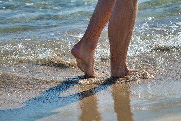 Photo detail of the wet feet of a boy walking along the coast of the sea on a sunny day. Concept of healthy living.