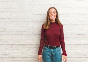 Young cool woman over a bricks wall funnny and friendly showing tongue