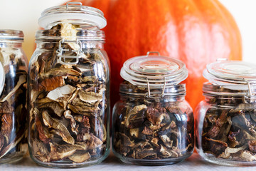 Autumn harvest. A delicacy of dried boletus in jars with a huge bright orange pumpkin in the background. EKO autumn Goodies. - obrazy, fototapety, plakaty