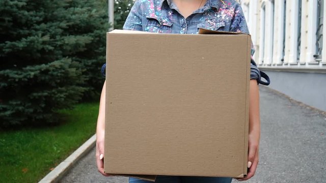 Woman carrying a cardboard box and walking outdoor
