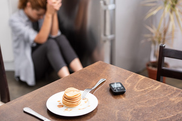 selective focus of tasty pancakes on table near glucose monitor and woman sitting on floor