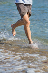 The lower part of a young man who is running on the shores of the beach wearing barefoot sportswear on the beach.