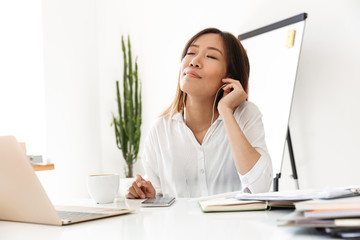 Fototapeta na wymiar Image of asian businesswoman listening to music with earphones in office